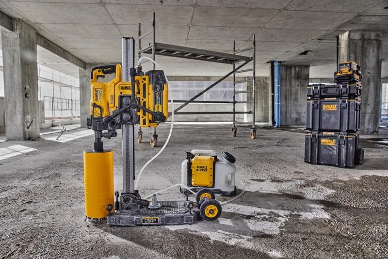 Una máquina de perforación DEWALT con un taladro cilíndrico amarillo, tanque de agua y cajas de almacenamiento negras está colocada sobre un suelo de hormigón en un sitio de construcción.
