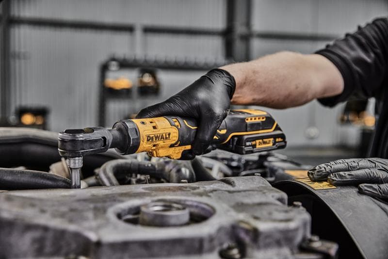 Una persona con guantes negros utiliza una herramienta de carraca inalámbrica DEWALT en un componente de motor en un taller.
