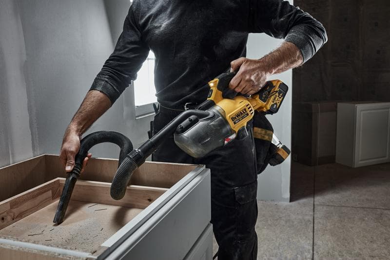 Una persona utiliza una aspiradora de mano inalámbrica DEWALT (modelo DCV501LN) para limpiar el aserrín de la superficie de un mueble de madera en un taller o durante una renovación.