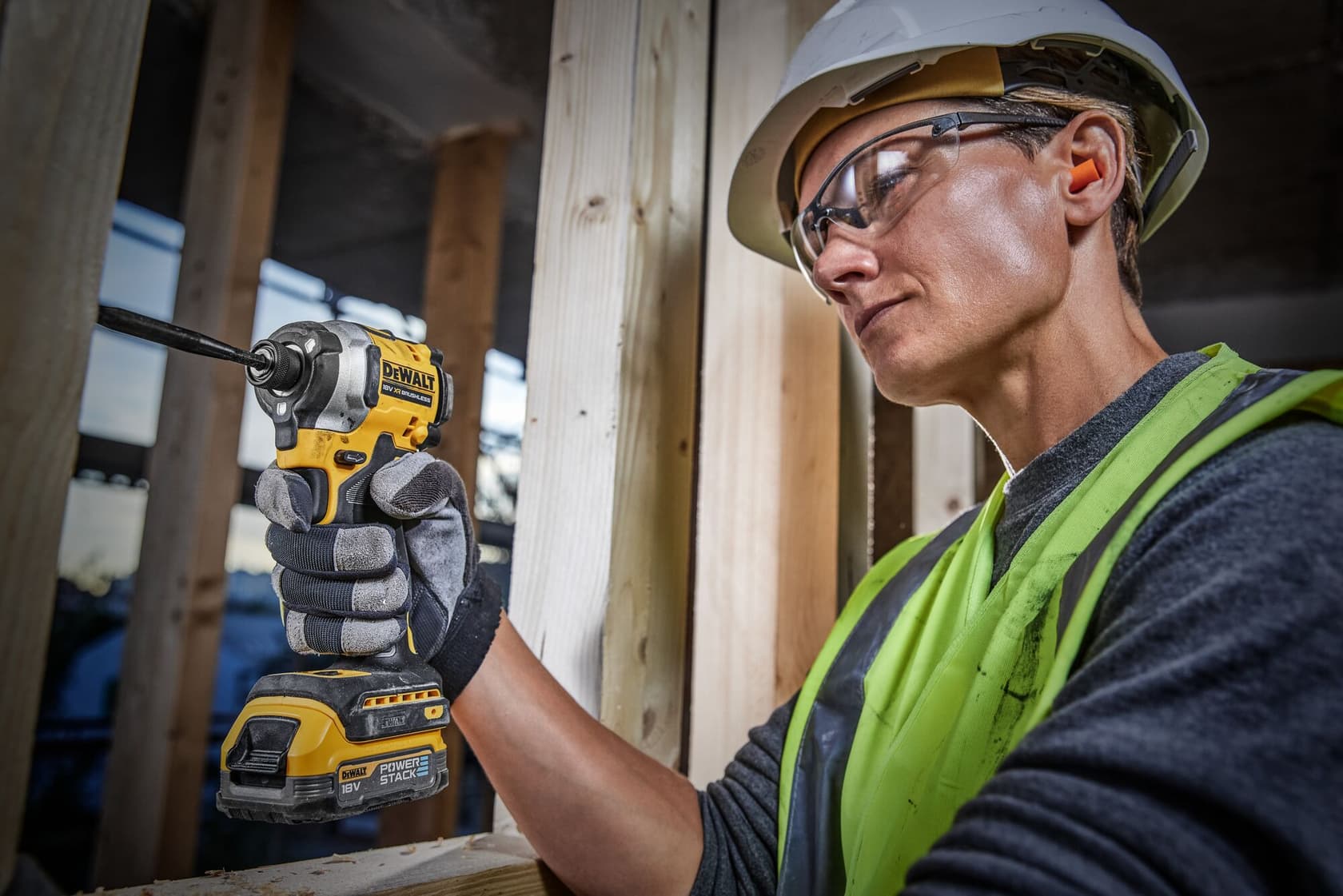 Persona con casco y chaleco de alta visibilidad utilizando una herramienta eléctrica inalámbrica DEWALT, concretamente un atornillador de impacto, en una obra de construcción.