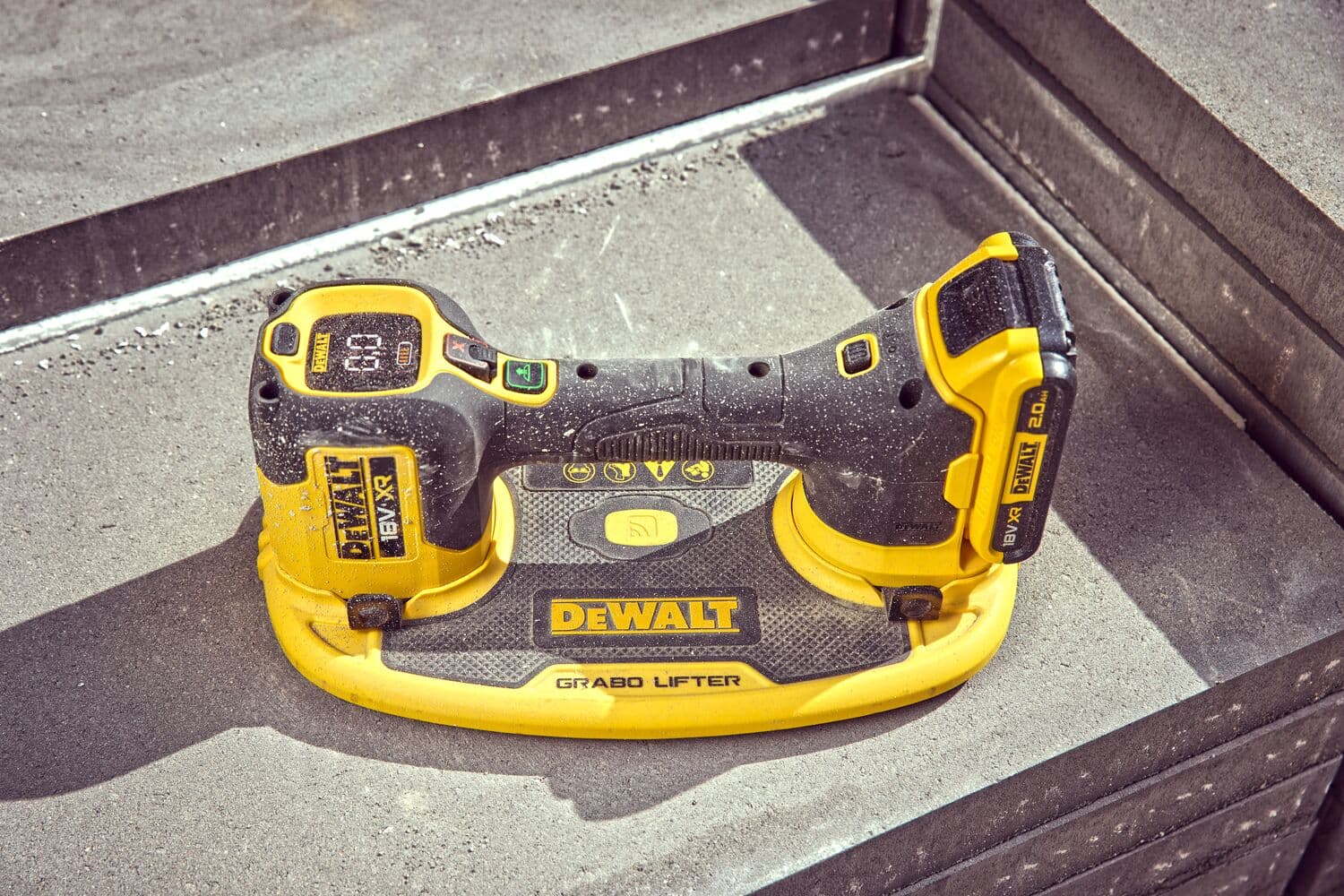 A DEWALT Grabo Lifter, a yellow and black cordless power tool designed for lifting and handling heavy materials, is placed on a concrete surface.