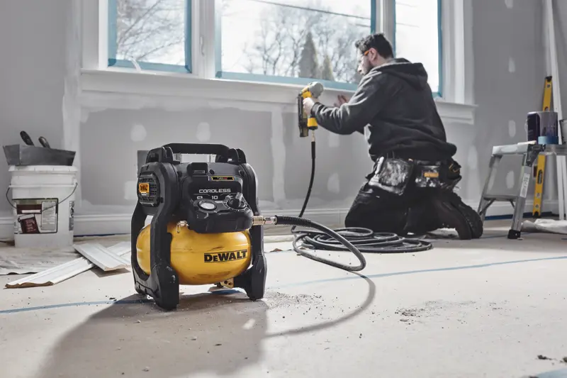 Compresor inalámbrico DEWALT en habitación renovada, trabajador usa clavadora cerca de la ventana.