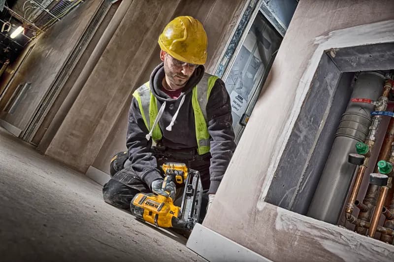 Trabajador con DEWALT DCN660N, casco amarillo y chaleco de seguridad en obra de construcción.