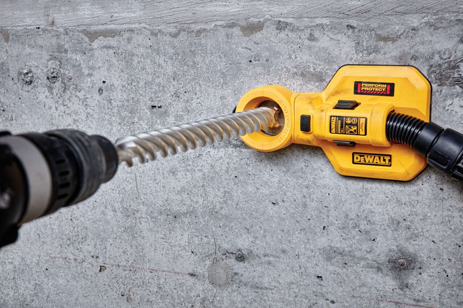 Un accesorio de extracción de polvo DEWALT se está utilizando con un taladro percutor para perforar una pared de hormigón. El accesorio recoge el polvo mientras se perfora, ayudando a mantener limpio el área de trabajo.
