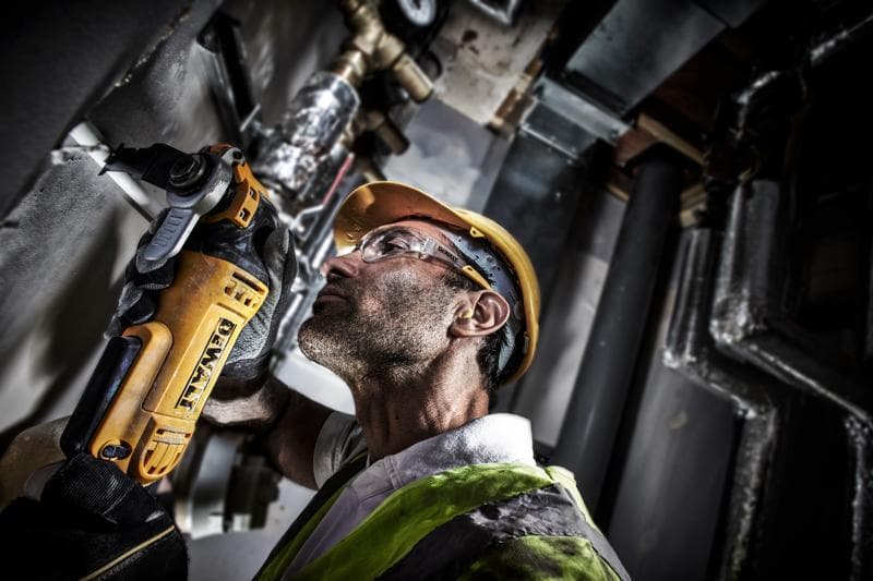 Un trabajador con equipo de seguridad utiliza una herramienta eléctrica DEWALT DWE315 para cortar una pared en un entorno industrial. El rostro del trabajador está difuminado para preservar la privacidad.
