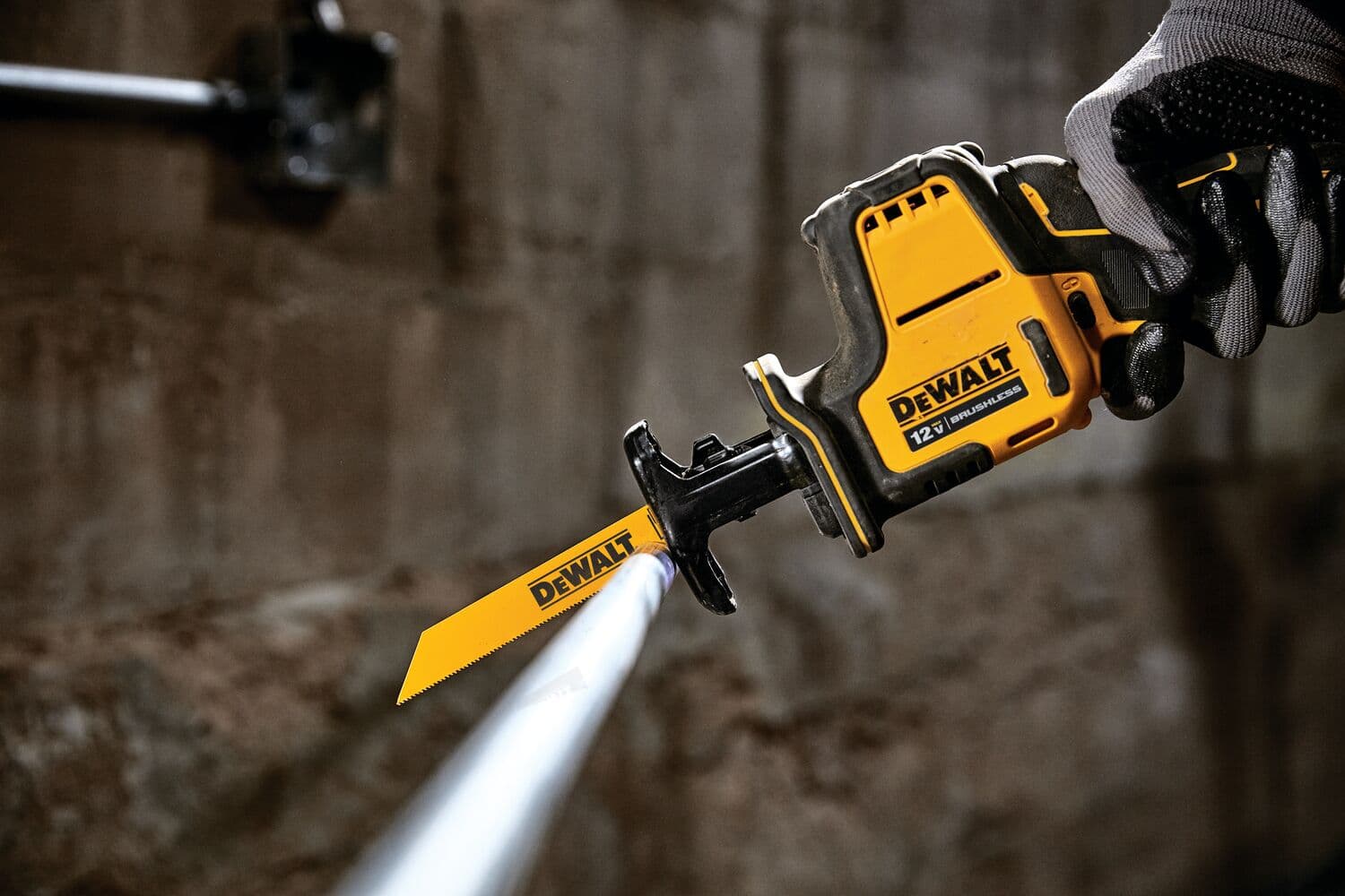 Una sierra recíproca DEWALT 12V utilizada para cortar una tubería de metal, sostenida por una mano enguantada en un entorno industrial.