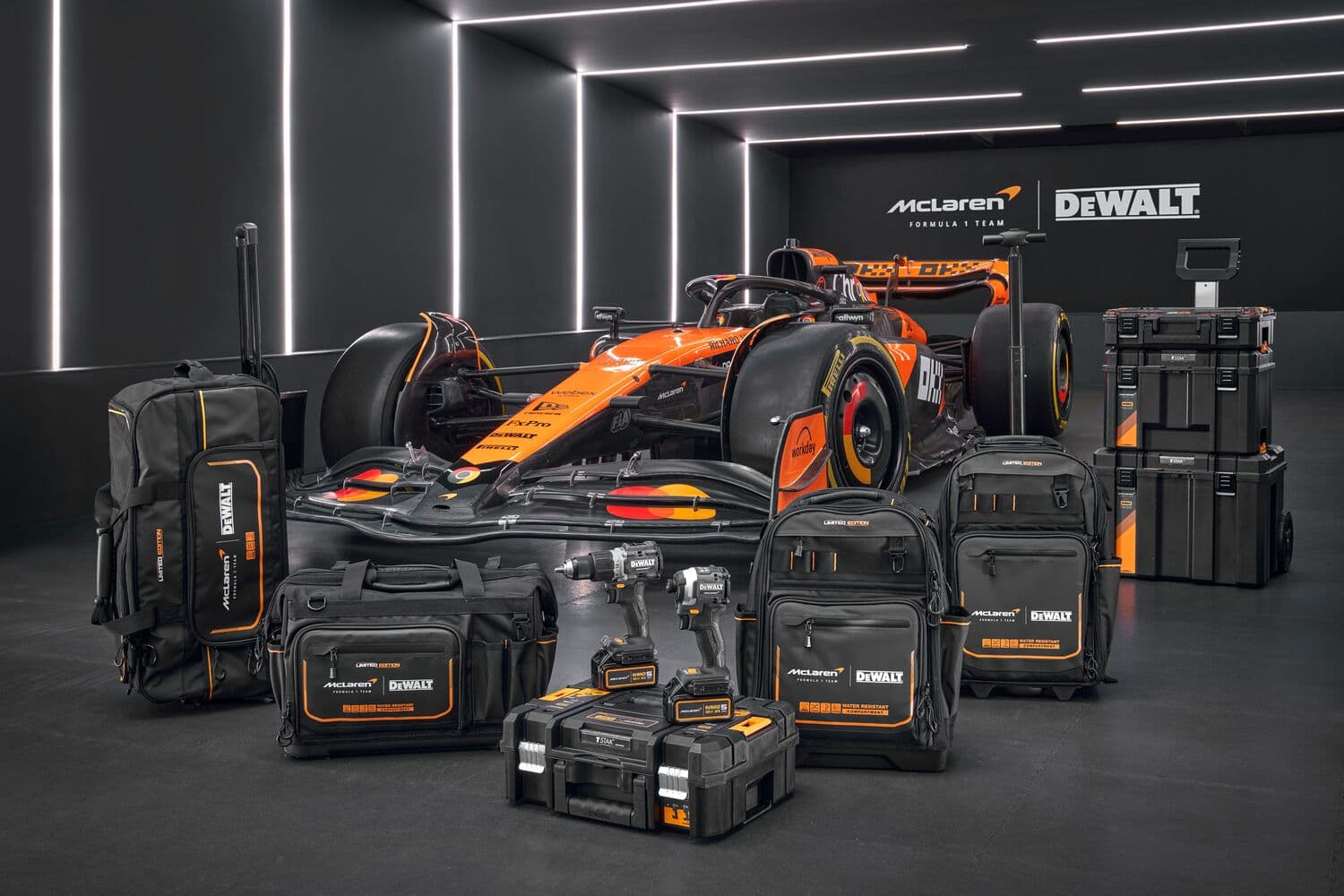 Un auto de carrera McLaren de Fórmula 1 se muestra en un garaje moderno iluminado, con una colección de bolsas para herramientas, herramientas eléctricas, mochilas y cajas de herramientas apilables de la marca DEWALT organizadas frente al vehículo.