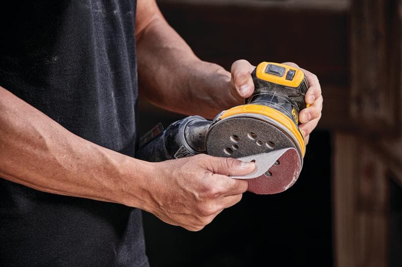 Primer plano de una persona colocando papel de lija en una lijadora orbital inalámbrica DEWALT.