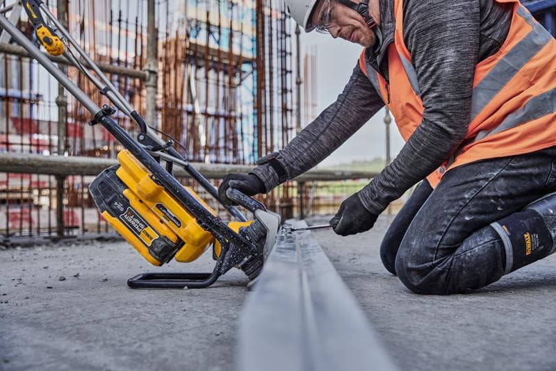 Una persona con equipo de seguridad de construcción utiliza una herramienta eléctrica inalámbrica DEWALT (SKU: DCPS330N) sobre una viga metálica en una obra.