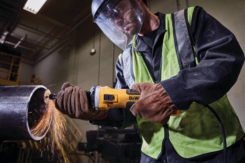 Una persona con equipo de protección y guantes usa una amoladora angular DEWALT para cortar un tubo metálico grande, con chispas saliendo de la zona de corte.