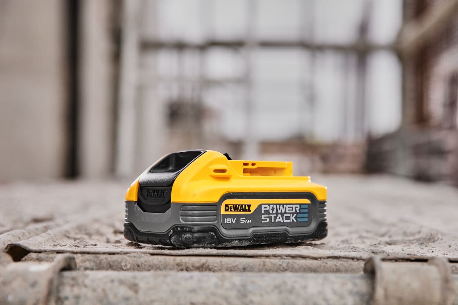 Módulo de batería DEWALT POWERSTACK 18V 5Ah colocado sobre una superficie de concreto rugosa, fotografiado en un entorno de construcción.