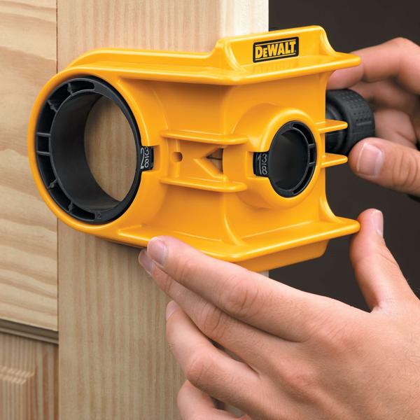 Una persona está utilizando un kit amarillo de instalación de cerraduras de puertas DEWALT para alinear y marcar un agujero en el marco de una puerta de madera.