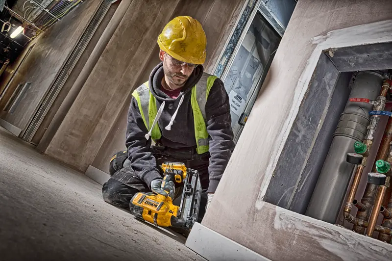 Trabajador con DEWALT DCN660N, casco amarillo y chaleco de seguridad en obra de construcción.