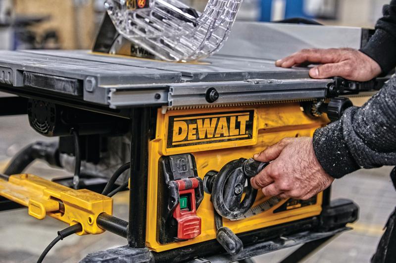 Primer plano de una persona ajustando la configuración de una sierra de mesa DEWALT, con un panel de control amarillo con interruptores y diales en un taller.