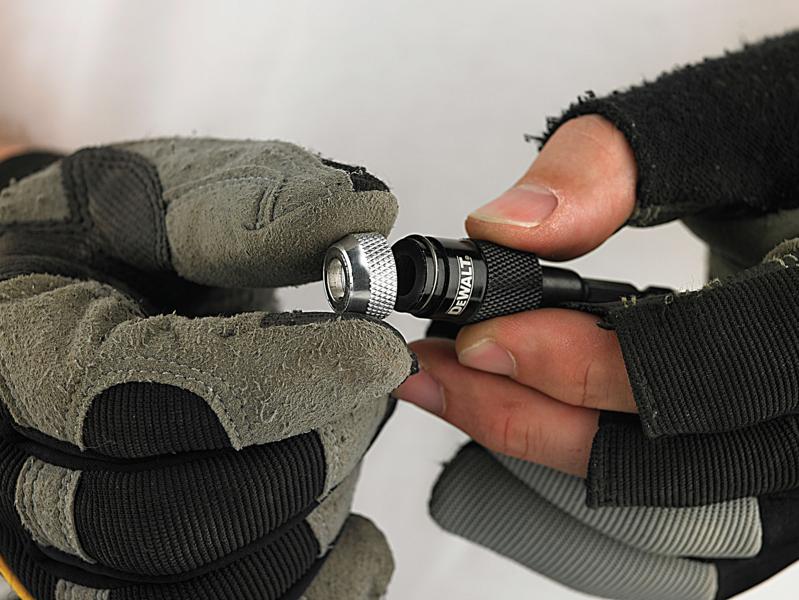 Primer plano de manos enguantadas sosteniendo un portabrocas DEWALT, mostrando el collar plateado texturizado y el cuerpo negro con el logotipo DEWALT.