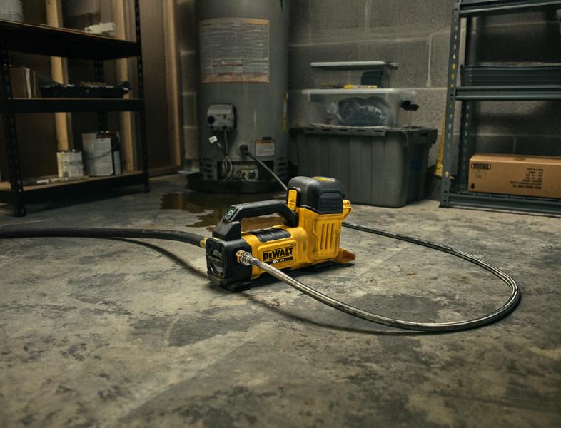 Una bomba de transferencia de agua portátil e inalámbrica DEWALT amarilla y negra (modelo DCE050N) con manguera conectada está colocada sobre un suelo de concreto en un taller o cuarto de servicio, rodeada de estanterías y cajas de almacenamiento.