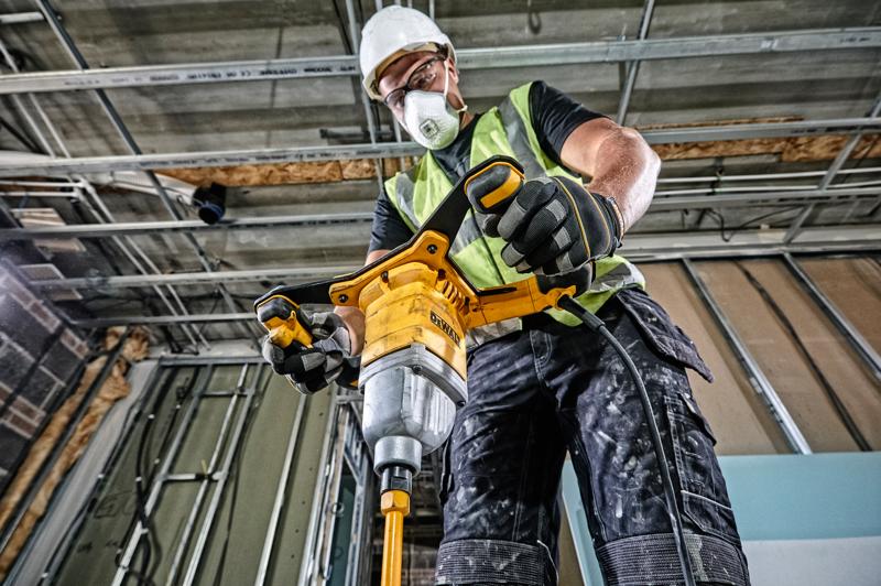 Un trabajador de la construcción con chaleco de seguridad, guantes y casco utiliza un taladro mezclador con cable amarillo DEWALT (DWD241) dentro de un edificio en construcción.