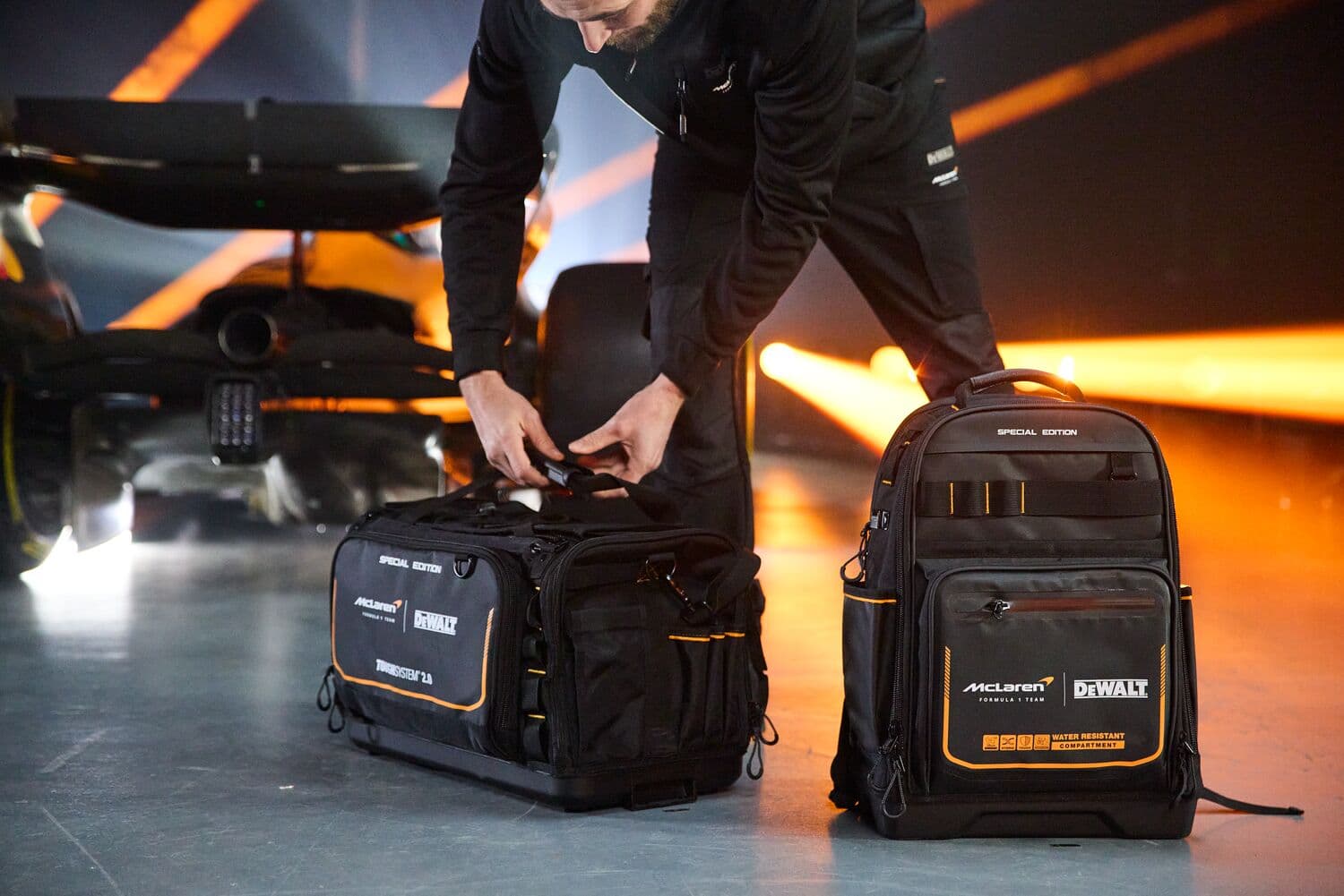 A person with DEWALT special edition tool bags near a race car; one is a duffel, one is a backpack.