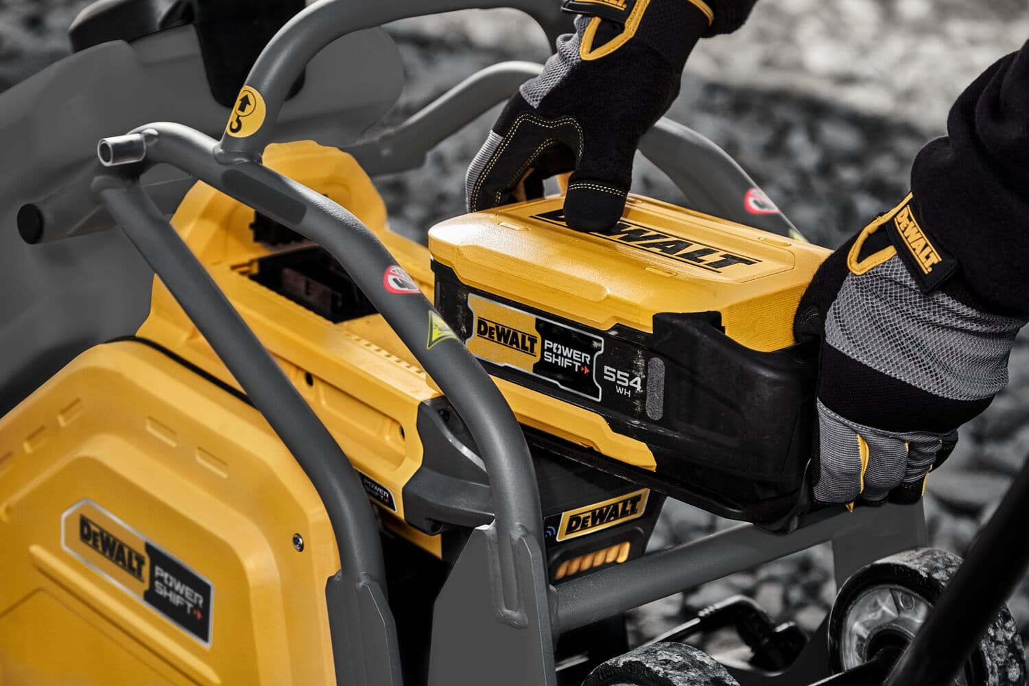 Primer plano de una persona con guantes instalando una batería DEWALT Power Shift en una máquina amarilla de equipos de energía exterior DEWALT.