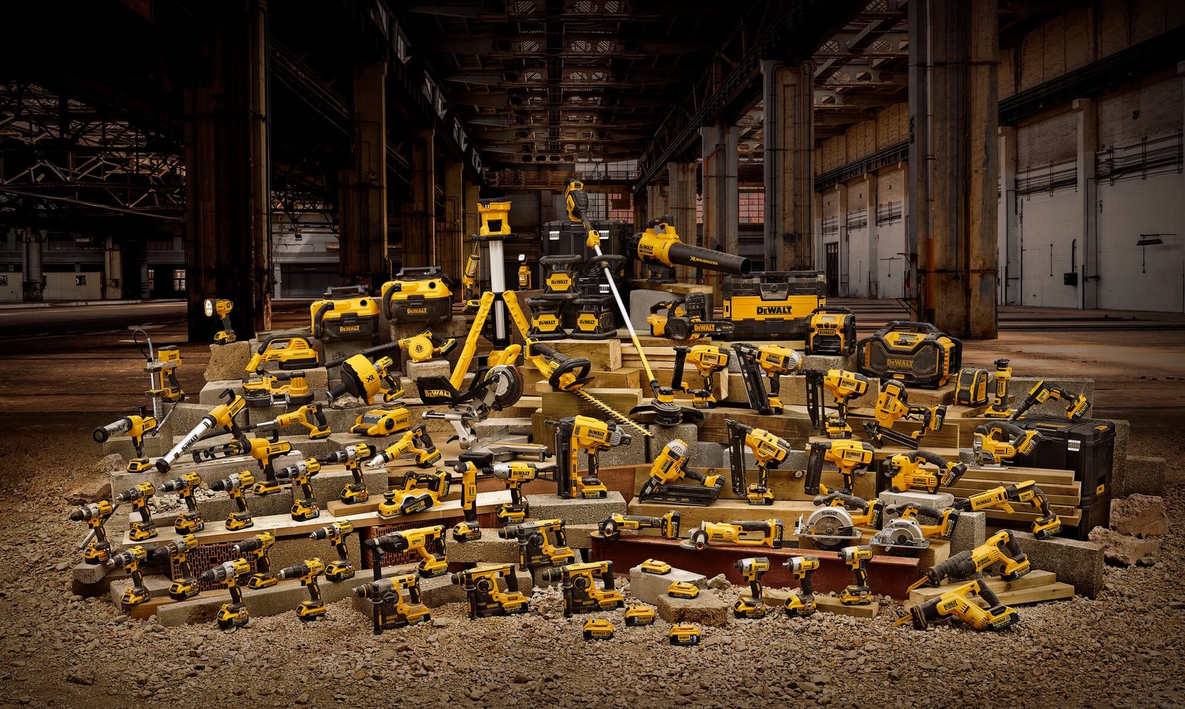 Una gran colección de herramientas eléctricas, accesorios y cajas de herramientas DEWALT organizadas sobre bloques de concreto en un entorno de almacén industrial. Las herramientas incluyen taladros, sierras, amoladoras y otros equipos de construcción, todos en los característicos colores amarillo y negro de DEWALT.