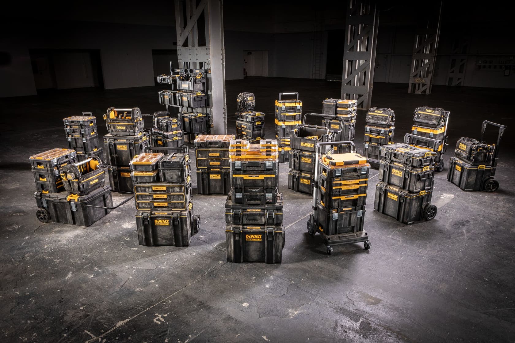 Varias unidades portátiles de almacenamiento y organización de herramientas DEWALT están dispuestas en un amplio entorno industrial. Las cajas negras y amarillas están apiladas y posicionadas en varias configuraciones, incluyendo unidades con ruedas y asas.