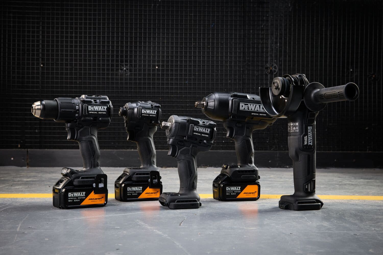 Four DEWALT power tools with batteries lined up on a concrete floor, photographed against a dark industrial background.