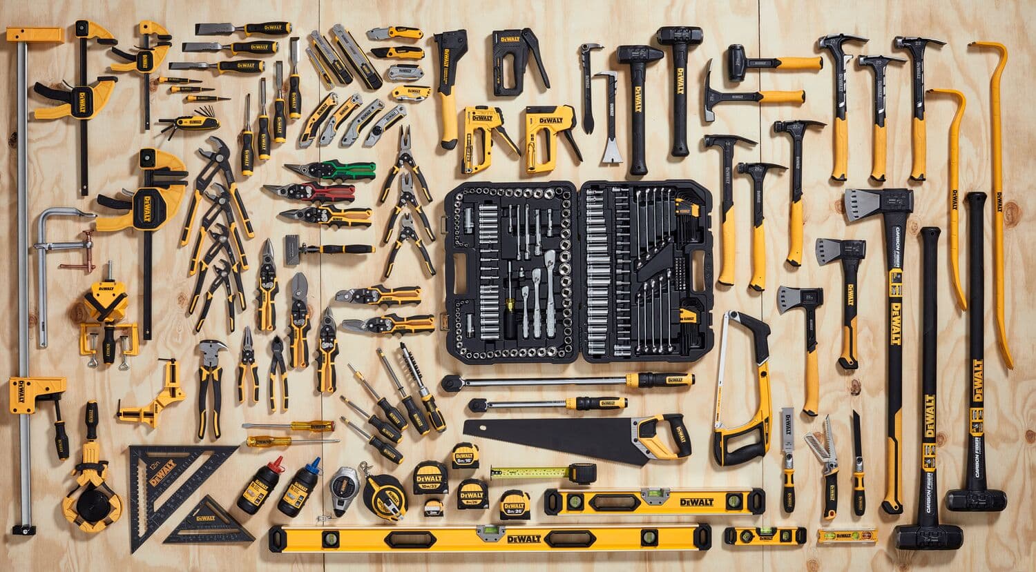 Una amplia variedad de herramientas manuales e instrumentos de medición DEWALT organizados cuidadosamente sobre una superficie de madera. La colección incluye martillos, alicates, destornilladores, llaves, cintas métricas, abrazaderas, niveles, sierras y un kit de herramientas con llaves de vaso y carracas, todos en colores amarillo y negro.